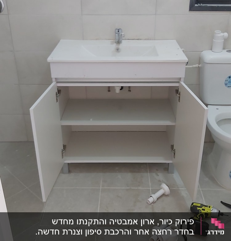 ארון פתוח עם כיור, כלי עבודה וצינורות על הרצפה